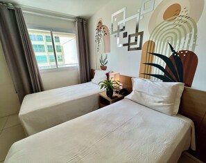 Una habitación de hotel con dos camas individuales, una mesita de noche con lámpara, un teléfono y una planta en maceta.