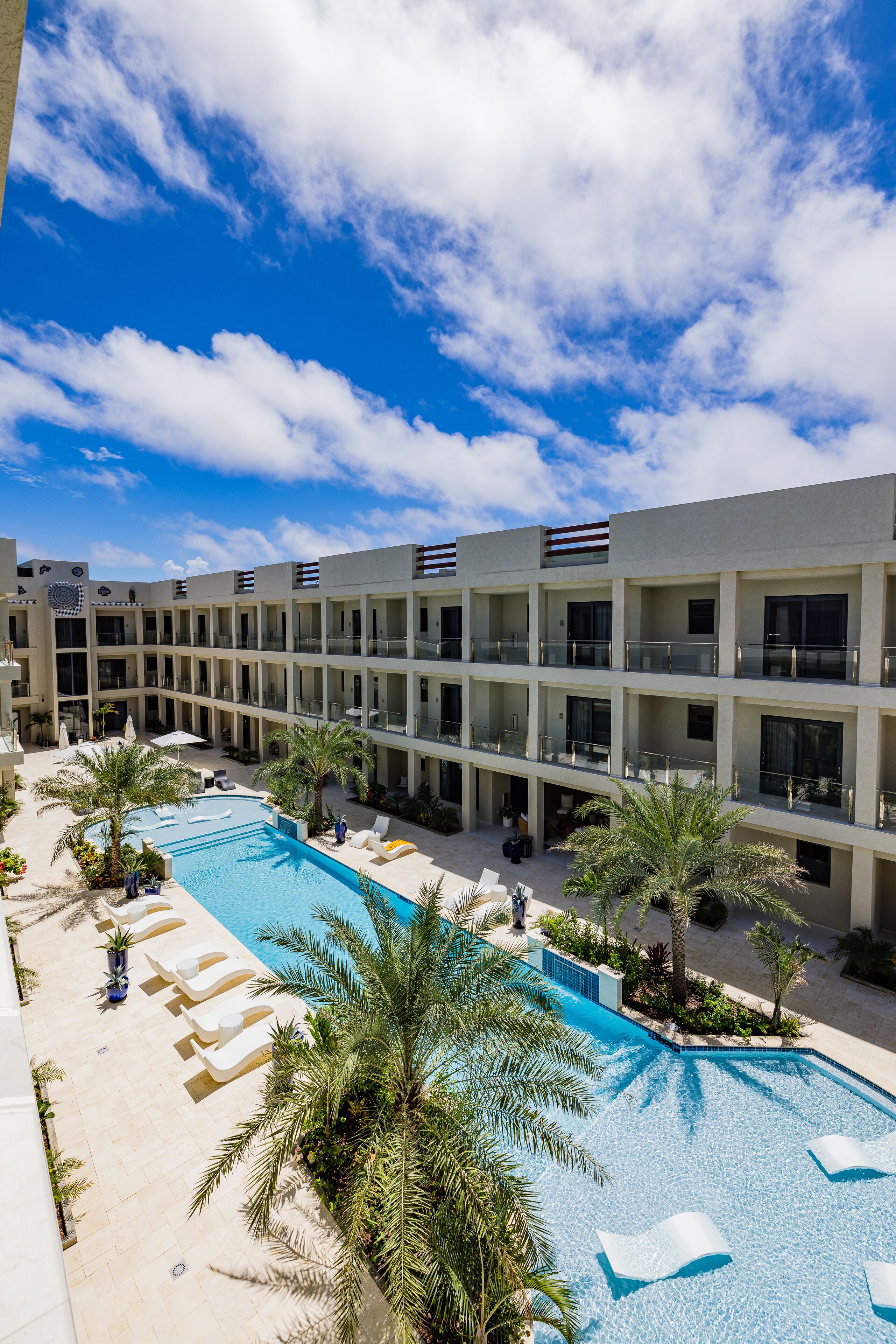 A hotel with a swimming pool, palm trees, and a clear blue sky.