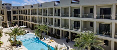 A hotel with a swimming pool, palm trees, and a clear blue sky.