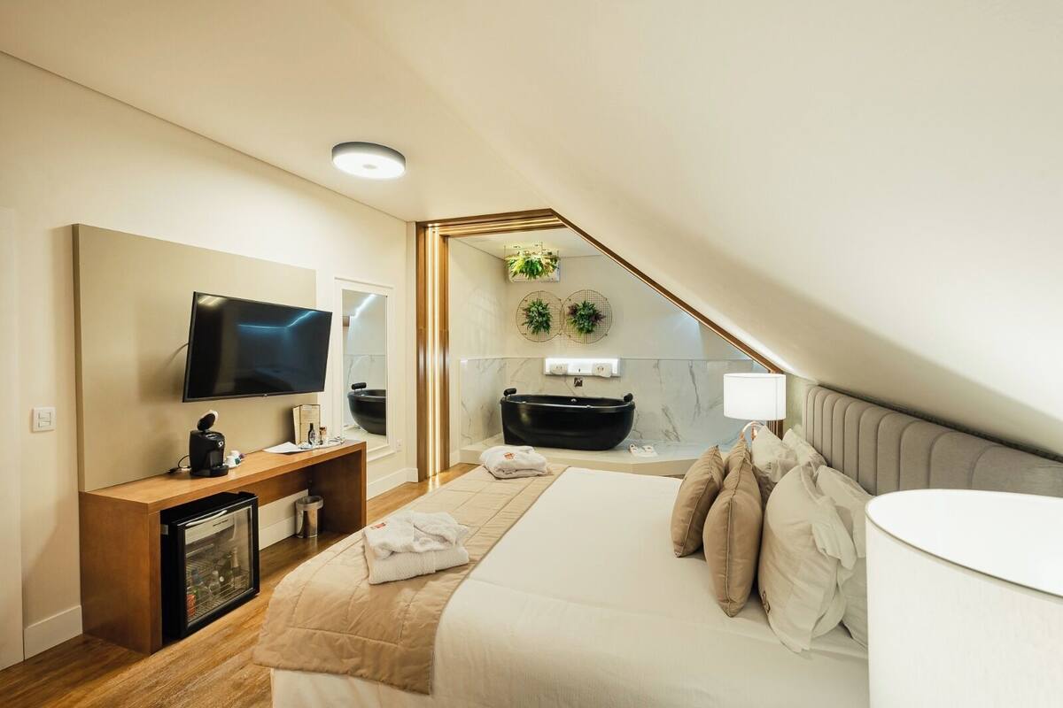 A modern bedroom with a large bed, a TV, a desk, and a bathtub.