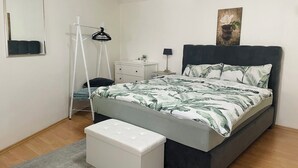 Une chambre à coucher avec un lit, une table de chevet, une commode, un miroir et un tableau accroché au mur.