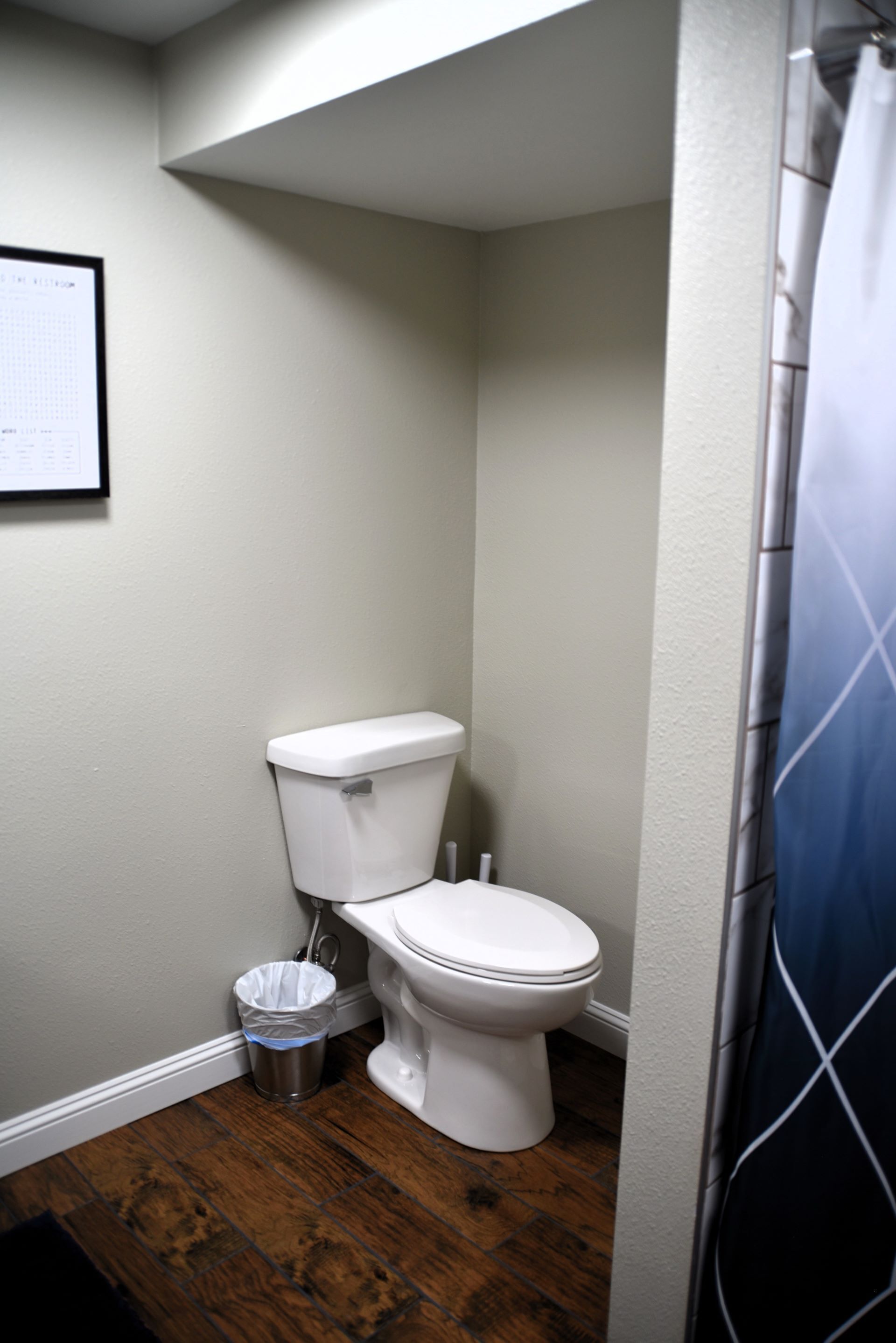 Une petite salle de bain avec des toilettes blanches, une poubelle et un rideau de douche.