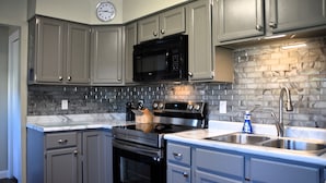 A kitchen with grey cabinets, a black microwave, a stainless steel oven, and a marble countertop. - At Home on South Canyon 
Newly remodeled Ranch home with plenty of space. (Rapid City)