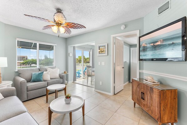 A living room with a ceiling fan, a TV, a sofa, a coffee table, and a view of the outdoors.
