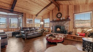 A cozy living room with a fireplace, wooden walls, and a leather sofa. - Chateau De Bjorne (Big Bear Lake)