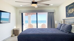 Un dormitorio con una cama grande, un ventilador de techo, vistas a la playa y una obra de arte enmarcada en la pared.