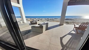 Un espacio de estar al aire libre cubierto, con mobiliario de mimbre y vista al mar.