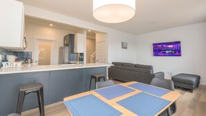 Ett modernt kök med en köksö i mitten, en matplats med ett träbord och ett vardagsrum med en soffa och en tv.