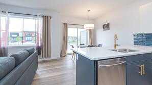 Ett modernt kök med en central köksö, en inbyggd diskmaskin och en matplats med bord och stolar.
