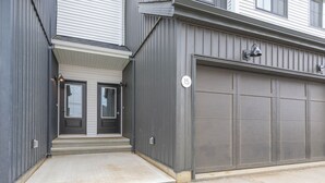 Ett garage som tillhör ett bostadshus, med en grå fasad och en vit garagedörr.