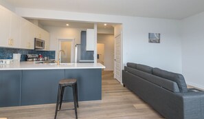 A modern kitchen with a central island, a grey sofa, and a wooden floor. - Beautiful Luxury Home (Edmonton)