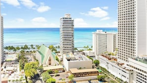 A high-rise hotel with a view of the ocean, a parking area, and a building with a unique roof structure.