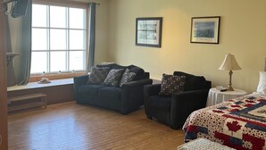 A room with a large window, two sofas, a bed with a quilt, and a lamp on a bedside table. - Hectors place (Twillingate)