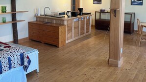 A spacious room with a wooden floor, a bed with a patterned bedspread, a wooden dresser, a kitchen area with a sink, a coffee maker, and a television mounted on a wooden stand. - Hectors place (Twillingate)