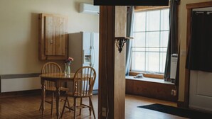 A wooden dining table with chairs, a vase with flowers, a wooden cabinet, and a window with curtains. - Hectors place (Twillingate)
