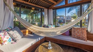 Un hamac suspendu entre deux fenêtres, d’où l’on peut admirer des palmiers et des maisons à l’extérieur.