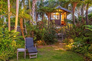 Una cabaña de madera con una escalera que conduce a un balcón, rodeada de exuberante vegetación tropical.