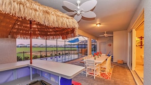 A modern outdoor dining area with a thatched roof, a white table, and a view of a green landscape.