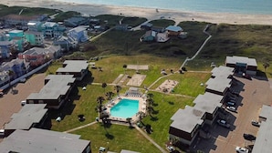 Vista aérea de una zona residencial costera con piscina, rodeada de casas y una playa al fondo.