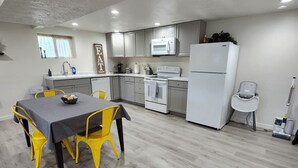 A modern kitchen with grey cabinets, a white refrigerator, and a dining area with a grey table and yellow chairs. - Spacious & Modern Guest Apartment with Private Entrance (Smithfield)