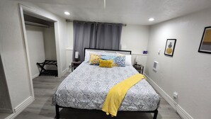A bedroom with a bed, a bedside table, a lamp, a window with curtains, and a wall-mounted air conditioner. - Spacious & Modern Guest Apartment with Private Entrance (Smithfield)