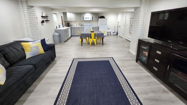 A modern living room with a sofa, a dining table with chairs, a kitchen area, and a television. - Spacious & Modern Guest Apartment with Private Entrance (Smithfield)