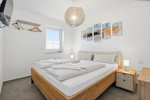 Une chambre à coucher comprenant un lit, des tables de chevet, un luminaire suspendu, une fenêtre et des œuvres d’art murales.