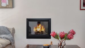 Una sala de estar con chimenea, un sofá, una mesa de centro con un jarrón de flores y un cuadro en la pared.