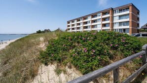A beachfront hotel with multiple balconies, a sandy beach, and a wooden fence. - Salzwasser - Modernes App. mit Balkon, Meerblick, Pkw-stellplatz, Wlan. Haustiere Erlaubt (List)