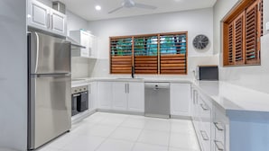 A modern kitchen with white cabinets, stainless steel appliances, a built-in oven, and a dishwasher. - Villa 3 @ Chez Willow (Port Douglas)