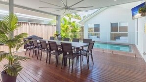 Uma área moderna para refeições ao ar livre com piscina, piso de madeira e ventiladores de teto.