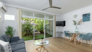 A modern living room with a grey sofa, a glass coffee table, and a dining area with teal chairs and a glass table. - Apartment 2 @ Ocean Palms Apartments (Douglas)