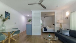 A modern living room with a glass dining table, a sofa, and a ceiling fan. - Apartment 2 @ Ocean Palms Apartments (Douglas)