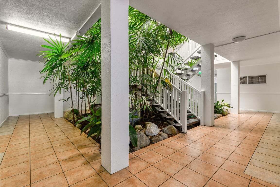 A spacious indoor area with a tiled floor, a staircase with a railing, and lush green plants.