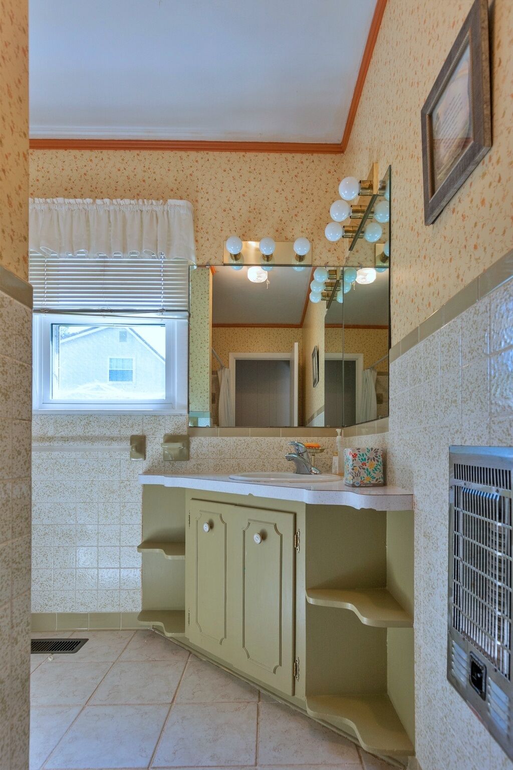 A bathroom with a window, vanity with a mirror, and a shower area.