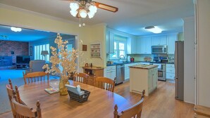 A spacious dining area with a wooden table and chairs, a ceiling fan, and a vase with flowers.