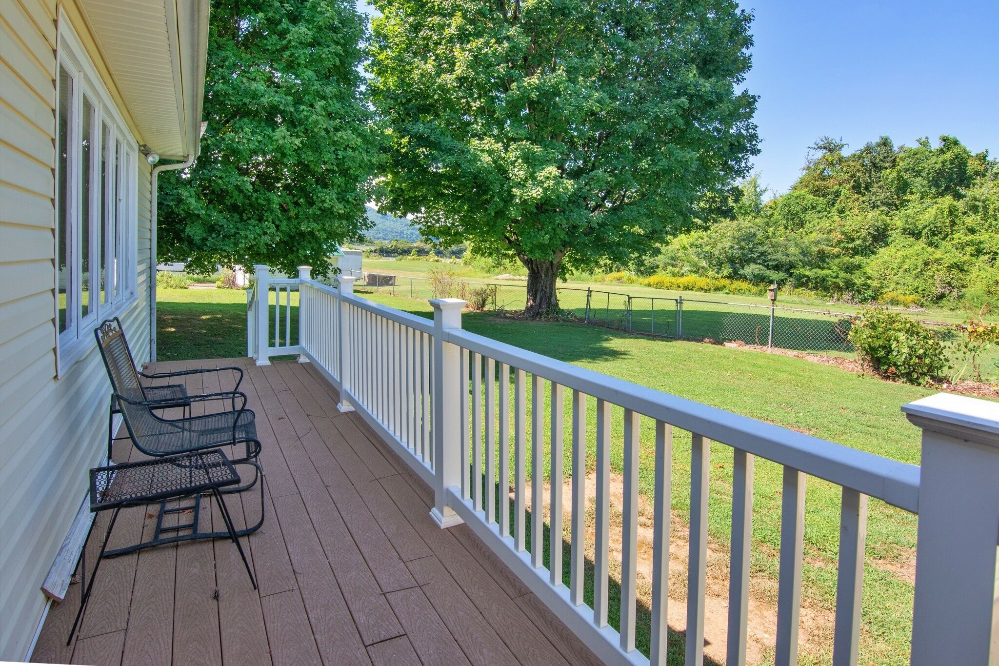 Un porche couvert avec une balustrade blanche, une chaise en métal et une vue sur une pelouse bien entretenue et des arbres.