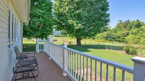A covered porch with a white railing, a metal chair, and a view of a well-maintained lawn and trees.