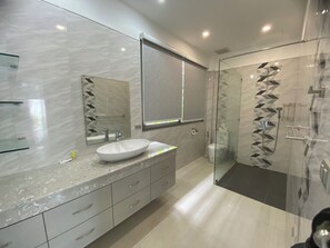 Une salle de bain moderne avec un grand miroir, un lavabo blanc et une douche à parois de verre.