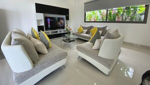 A modern living room with two sofas, a flat-screen TV, and a large window with a view of greenery. - Villa Oasis Tranquille 3 Chambres Avec Piscine (Rawai)