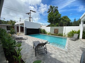 Une piscine extérieure moderne, dotée d’une terrasse carrelée, de chaises longues et d’un mur en pierre.