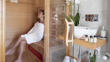 Relax in a serene spa room with a glass-enclosed sauna, sink, and mirror.