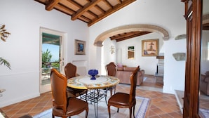 A dining area with a round table, four chairs, and a blue decorative bowl. There is a wooden ceiling and a brick fireplace in the background.