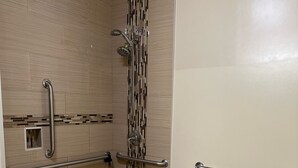 A bathroom with a shower, toilet, and grab bars. - Crystal Palace Inn (Maywood)