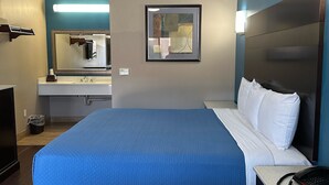 A hotel room with a large bed, a desk with a phone, a mirror, a sink, and a trash bin. - Crystal Palace Inn (Maywood)