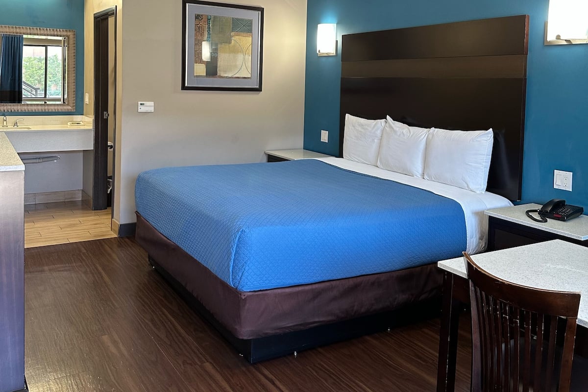 A hotel room with a large bed, a desk, a chair, a framed picture on the wall, and a window with curtains.