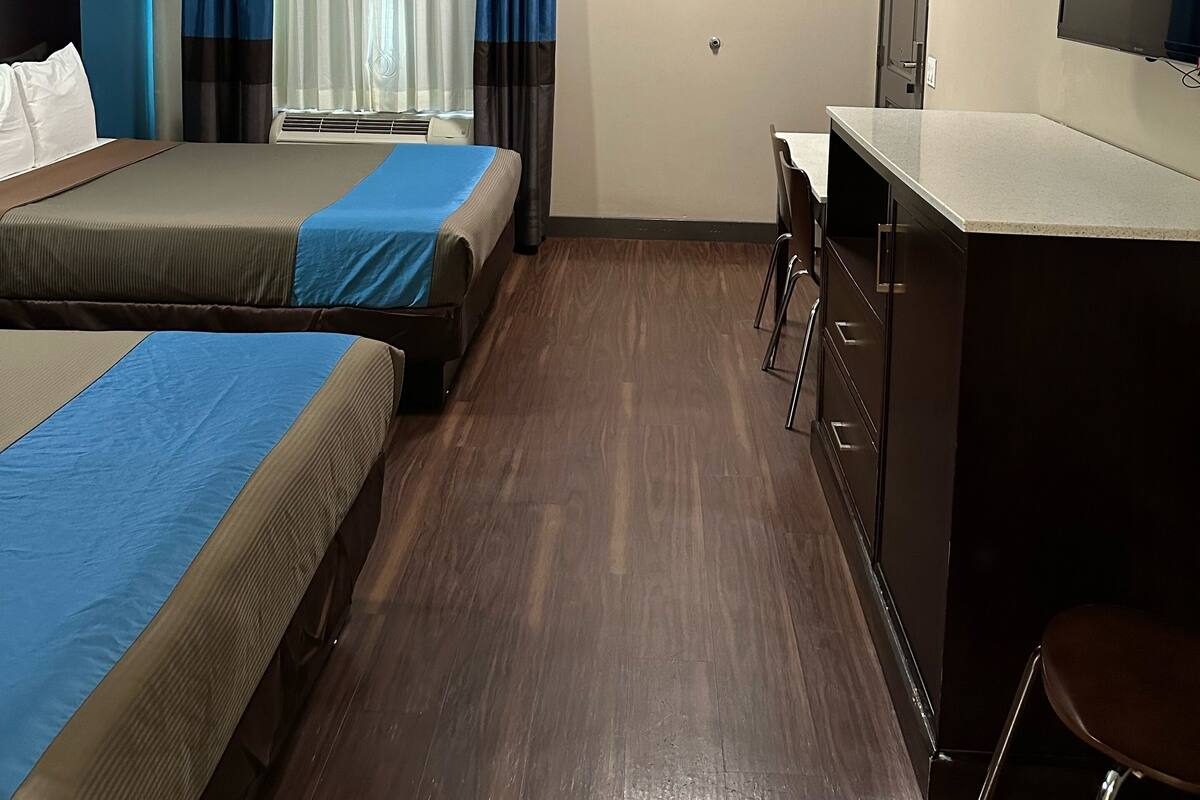 A hotel room with two beds, a desk, a chair, a television, and a window with curtains.