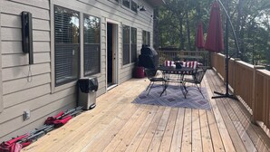 Una terraza de madera con una mesa, sillas, una parrilla y sombrillas.