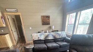 Una sala de estar con un sofá gris oscuro, piso de madera y una ventana con persianas.