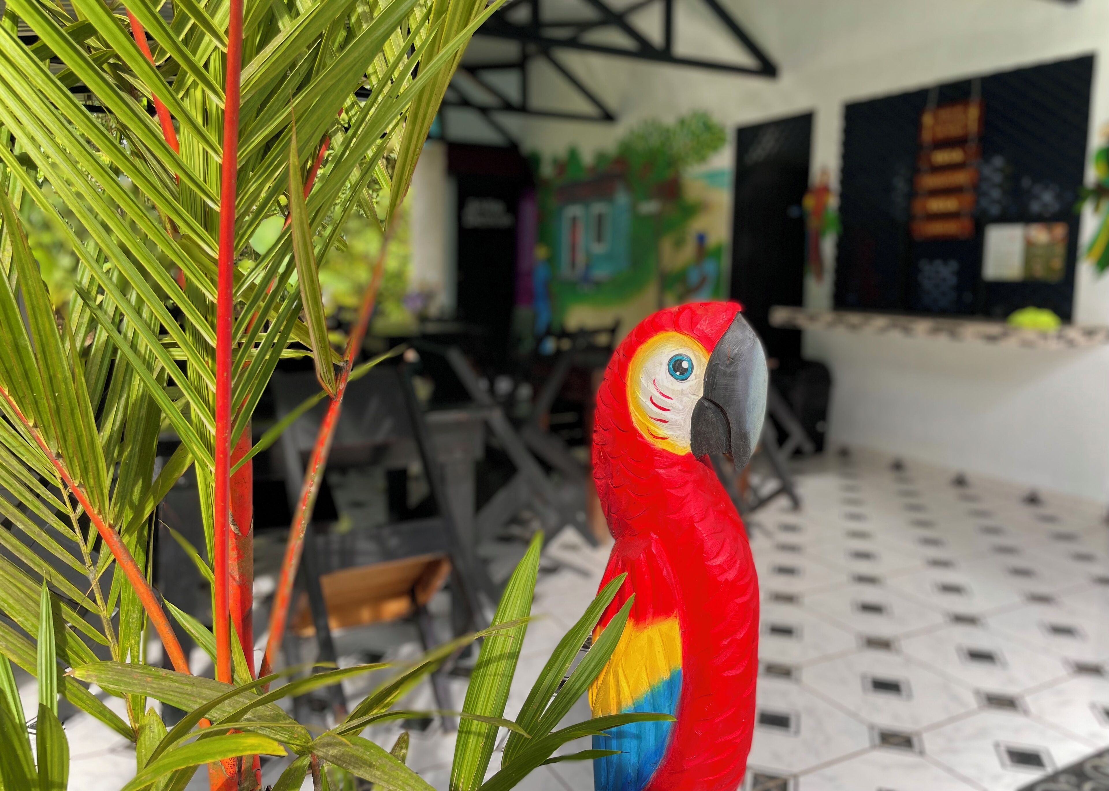A red and yellow parrot in a room with a tiled floor and a mural on the wall.